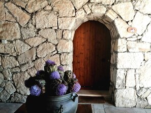 A stone wall with a wooden door and a pot of purple flowers. - Guney Urla Suites (Urla)