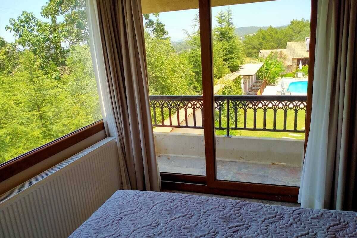 Una stanza con un letto, vista su un balcone con piscina e vegetazione all'esterno.