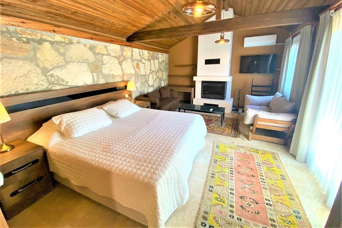 Una camera accogliente con parete in pietra, un letto con copripiumino bianco, un camino e un angolo salotto con tappeto decorato.