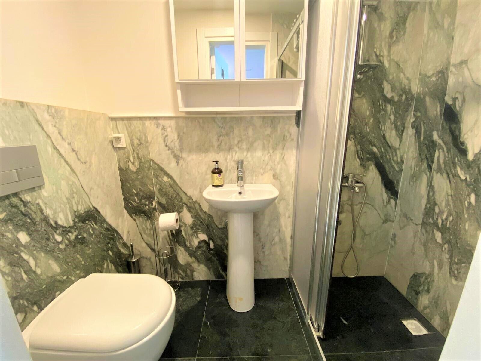 A bathroom with a white pedestal sink, a toilet, and a shower area.