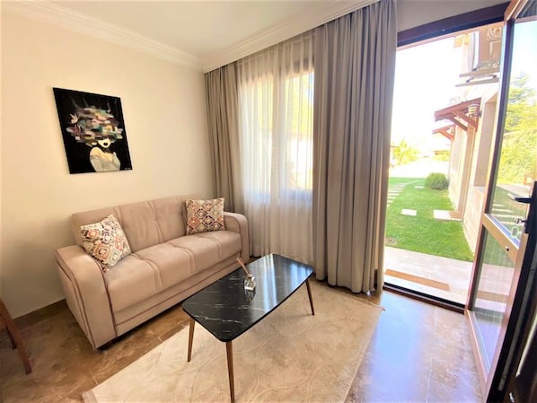 A living room with a beige sofa, a black coffee table, and a painting on the wall. - Guney Urla Suites (Urla)