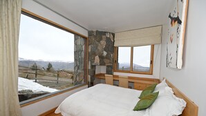 A bedroom with a large window, a stone wall, a bed with white and green pillows, and a wooden headboard. - Luxury chalet with best skiing in the South American Andes (farellones)
