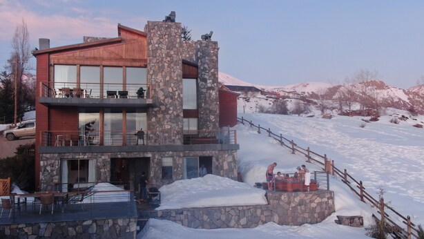 A modern two-story building with a stone facade, large windows, and a balcony with outdoor seating. - Luxury chalet with best skiing in the South American Andes (farellones)