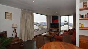 A modern living room with a large window, a television, a wooden coffee table, and a sofa.
