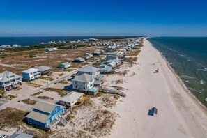 A coastal area with beach houses aligned along the shore, a clear sky, and the ocean in the background.