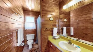 A wooden cabin bathroom with a toilet, sink, and mirror.