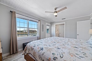 Een slaapkamer met een groot bed, een plafondventilator, een raam met gordijnen en uitzicht op de omgeving.