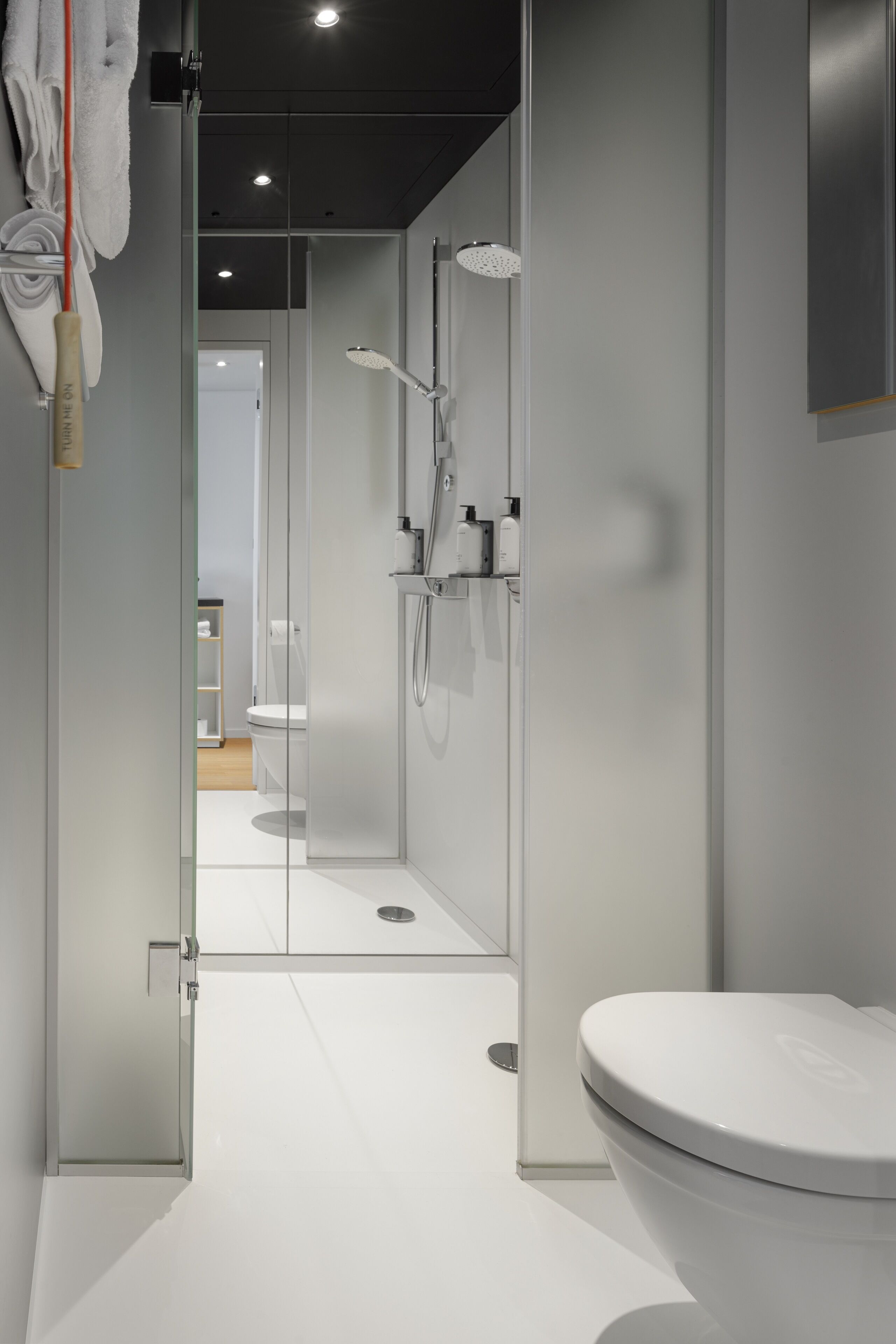 Un baño moderno con ducha acristalada, inodoro blanco y dispensador de papel higiénico a la vista.