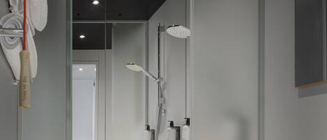 Un baño moderno con ducha acristalada, inodoro blanco y dispensador de papel higiénico a la vista.