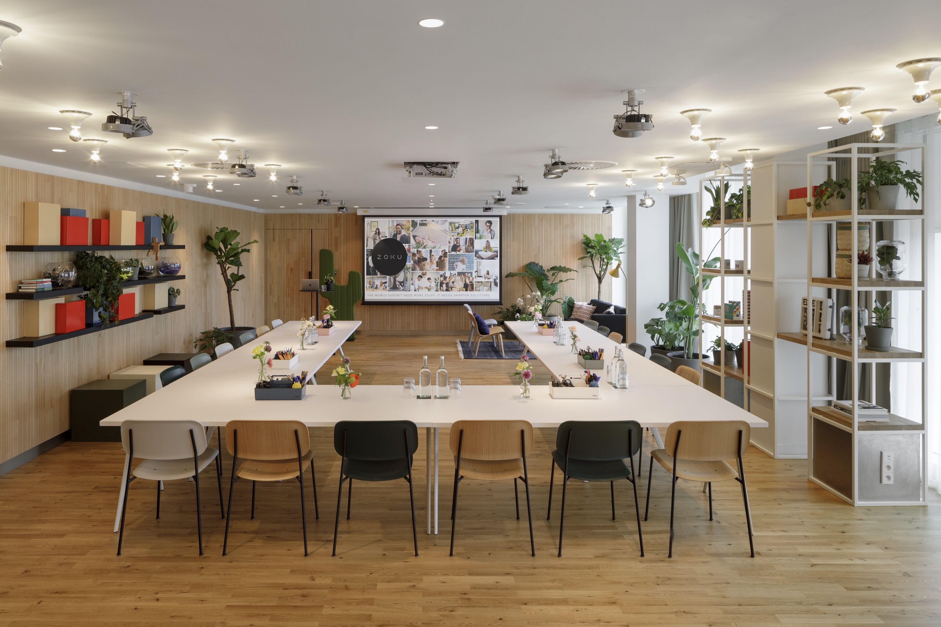 A modern conference room with a long table, multiple chairs, and a large screen displaying a presentation.