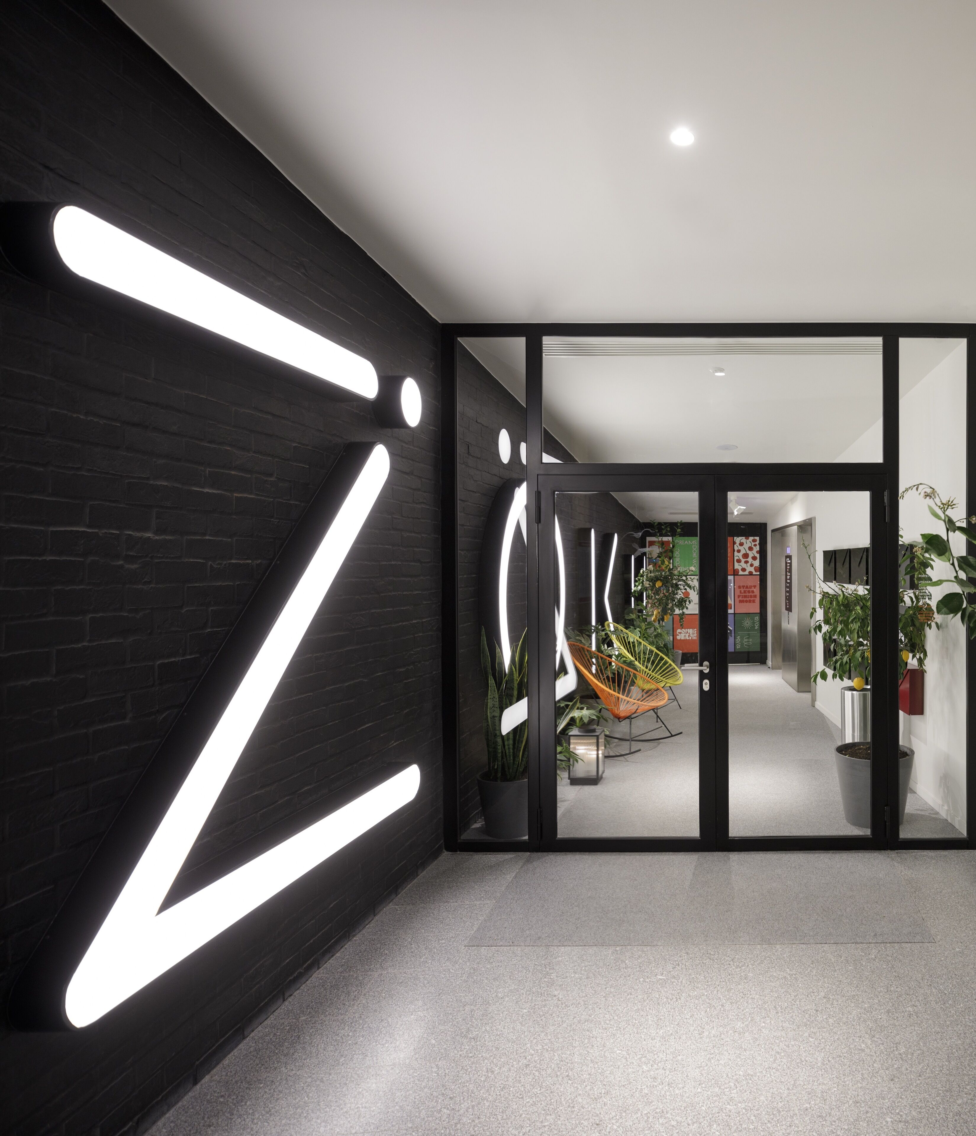 A modern interior with a black brick wall, a glass door leading to a hallway, and a potted plant.