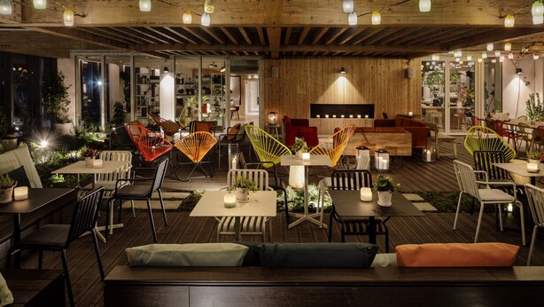 Un espace de restauration en plein air avec des tables et des chaises en bois, des guirlandes lumineuses et un plafond en bois.