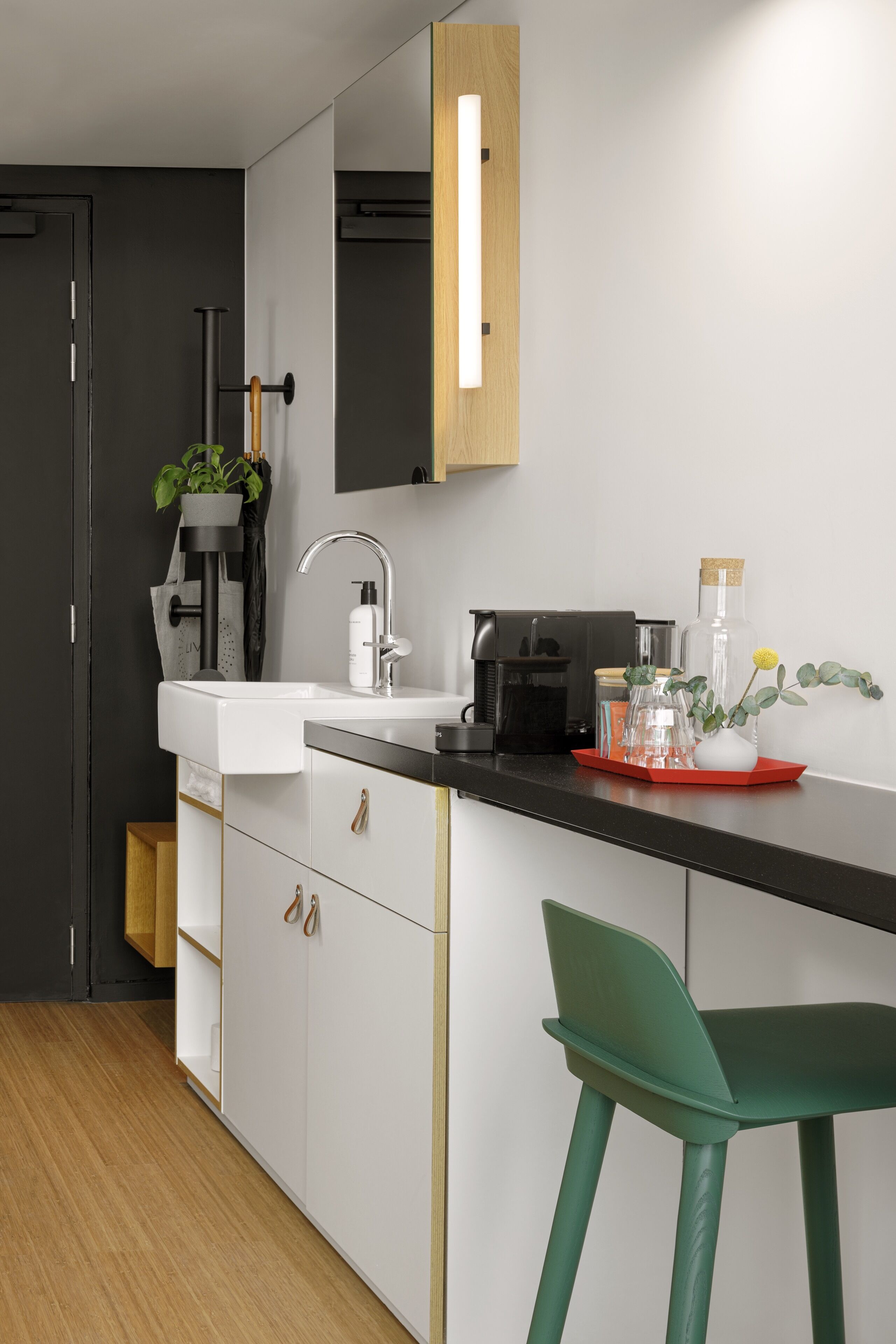A modern kitchen with a white sink, black countertop, and a green bar stool.