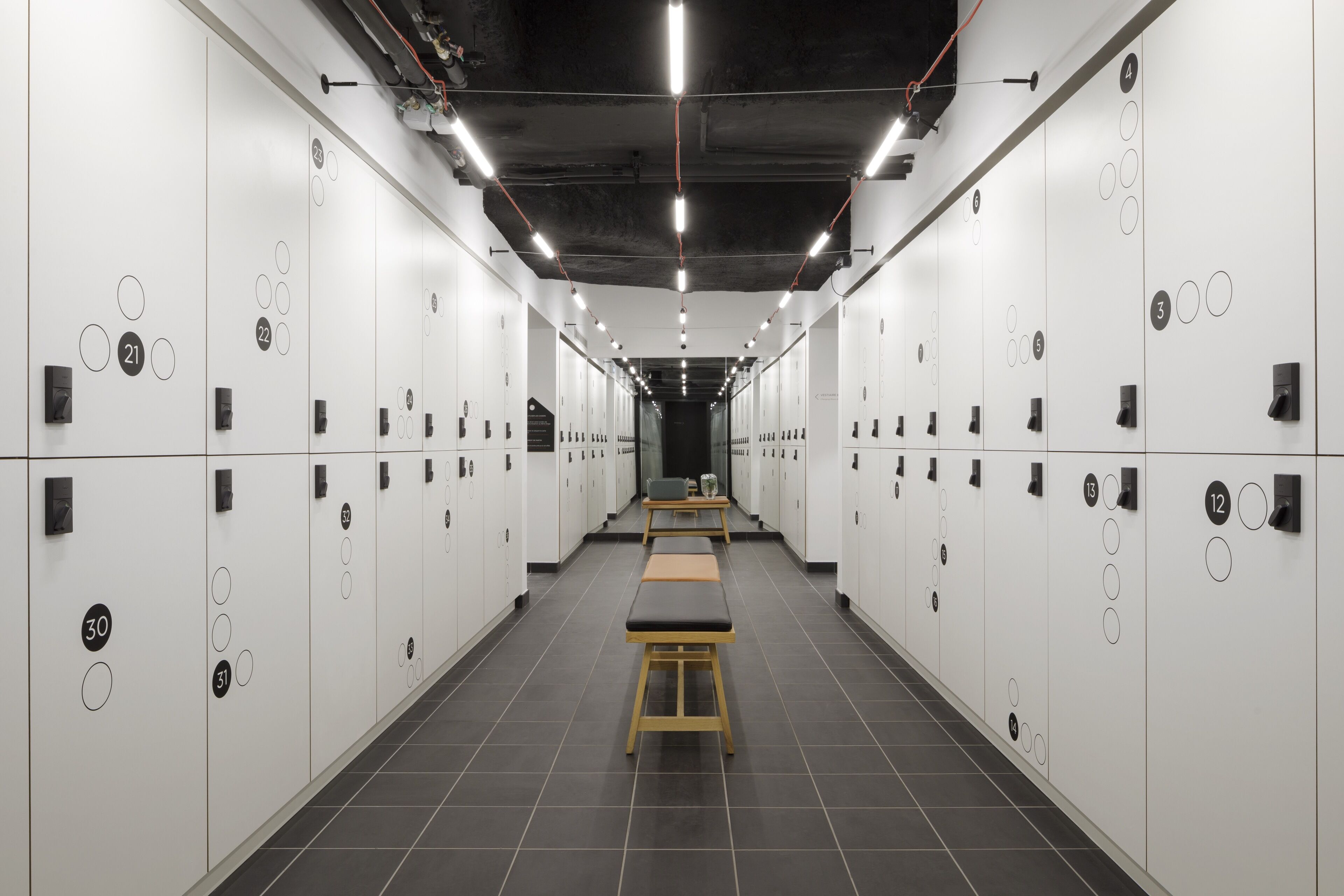 A row of white lockers with numbers, a bench in the center, and a tiled floor.