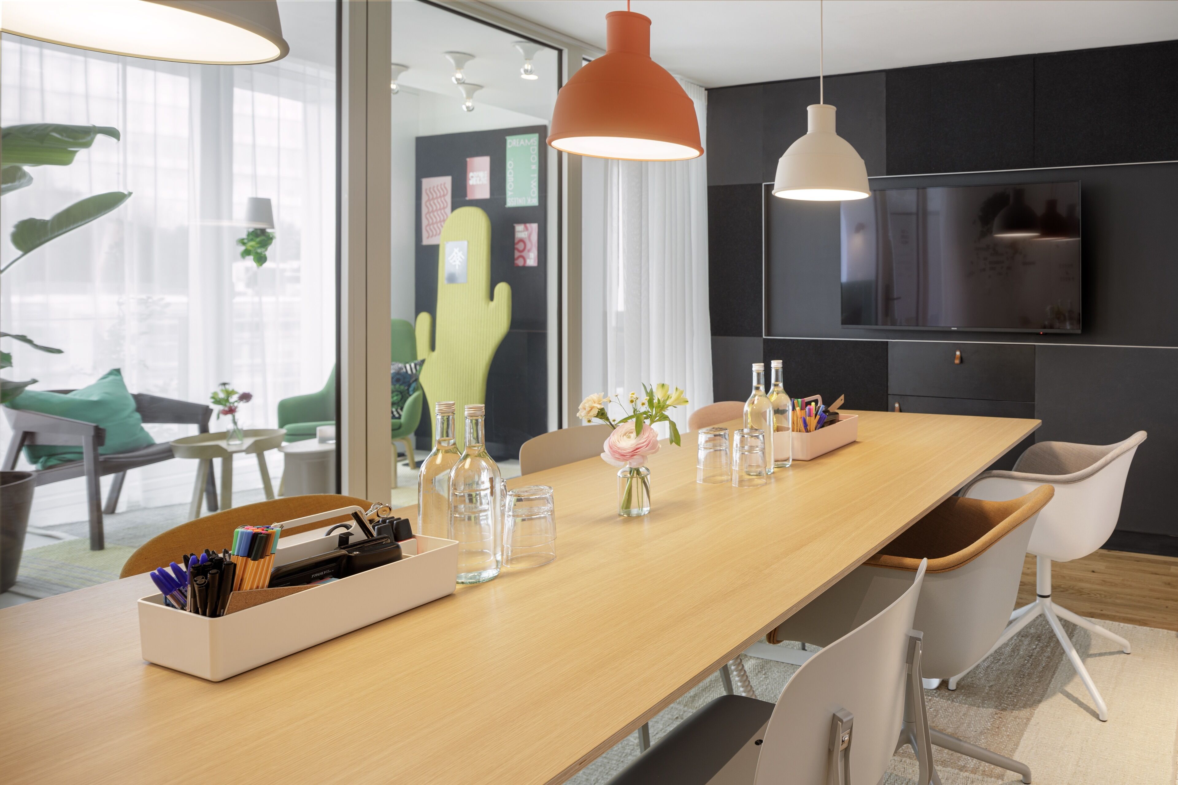 Un espace de bureau moderne avec une longue table en bois, des chaises et un téléviseur fixé au mur.