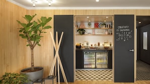 Un intérieur moderne avec un mur en bois, une plante en pot, un tableau noir sur lequel est inscrite une citation inspirante, et un coin cuisine avec des étagères et un réfrigérateur.