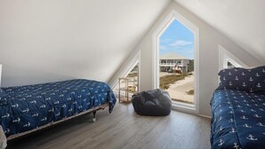 Ein Schlafzimmer mit zwei Betten, einem Sitzsack und einem großen Fenster mit Blick auf ein Gebäude und den Strand.
