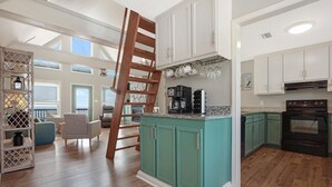 Eine geräumige Küche mit türkis-farbenen Schränken, einer Holztreppe und einem Essbereich mit blauen Stühlen.