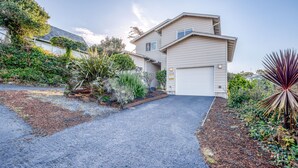 A two-story house with a driveway leading to a garage. - Pacific Peeks 2 - Oceanview Pet Friendly Retreat with EV Charging (fee) (Lincoln City)