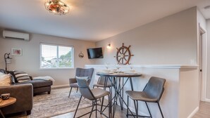 A modern living room with a round table, bar stools, a TV, and a sail wheel decoration. - Pacific Peeks 2 - Oceanview Pet Friendly Retreat with EV Charging (fee) (Lincoln City)