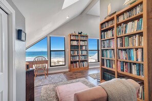 A spacious room with a large bookshelf, a cozy seating area, and a view of the ocean.