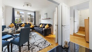 Ein modernes Wohnzimmer mit einer Couch, Sesseln, einem Couchtisch und einem Teppich. Eine Tür führt in einen anderen Raum.