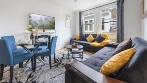 Ein modernes Wohnzimmer mit einem schwarzen Sofa, blauen Sesseln, einem Couchtisch und einem großen Fenster mit Vorhängen.