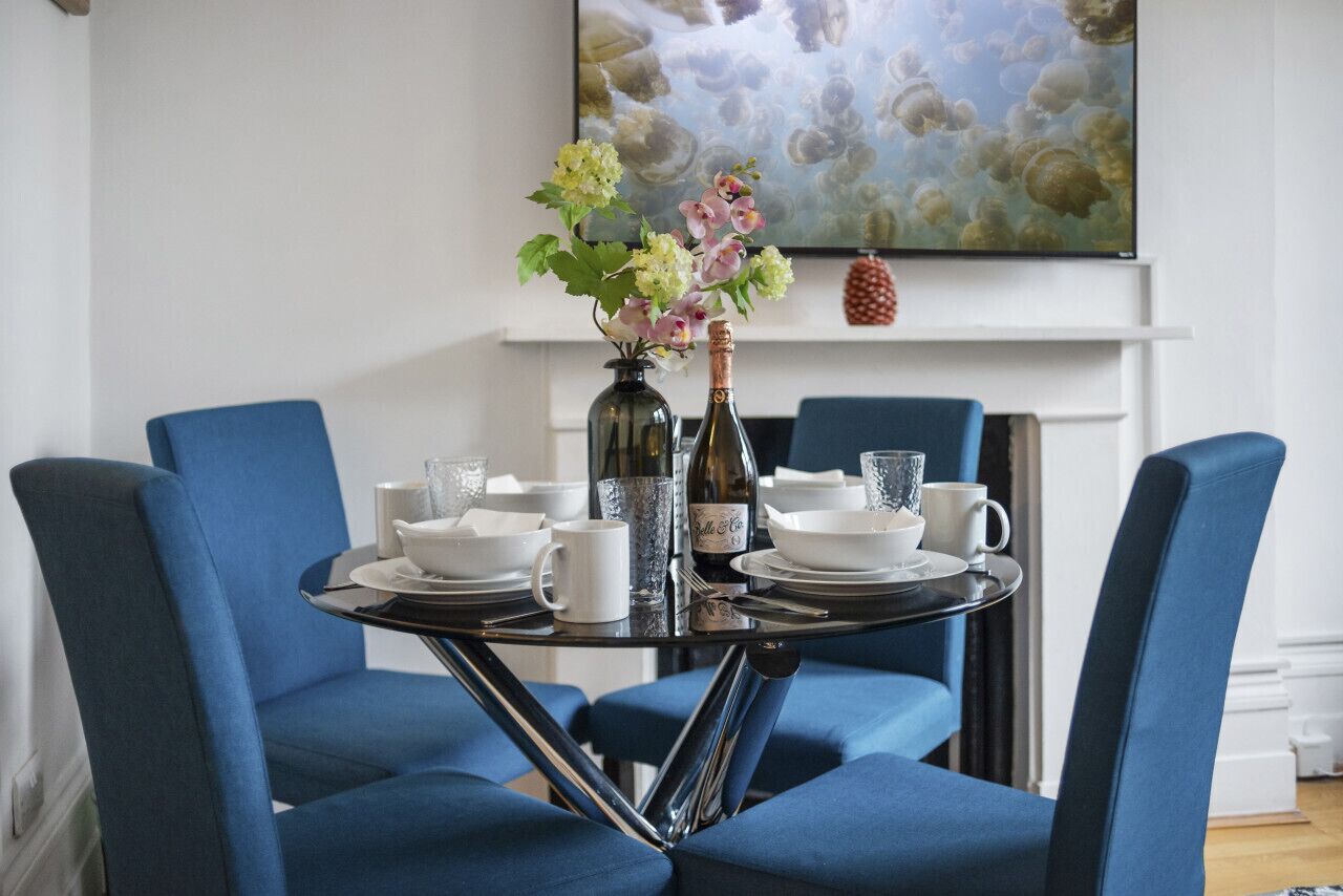 A dining table set with white plates, bowls, and cups, surrounded by blue chairs.