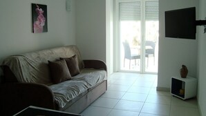 En stue med sofa, fjernsyn, et lille bord og en skydedør til et udendørs område.