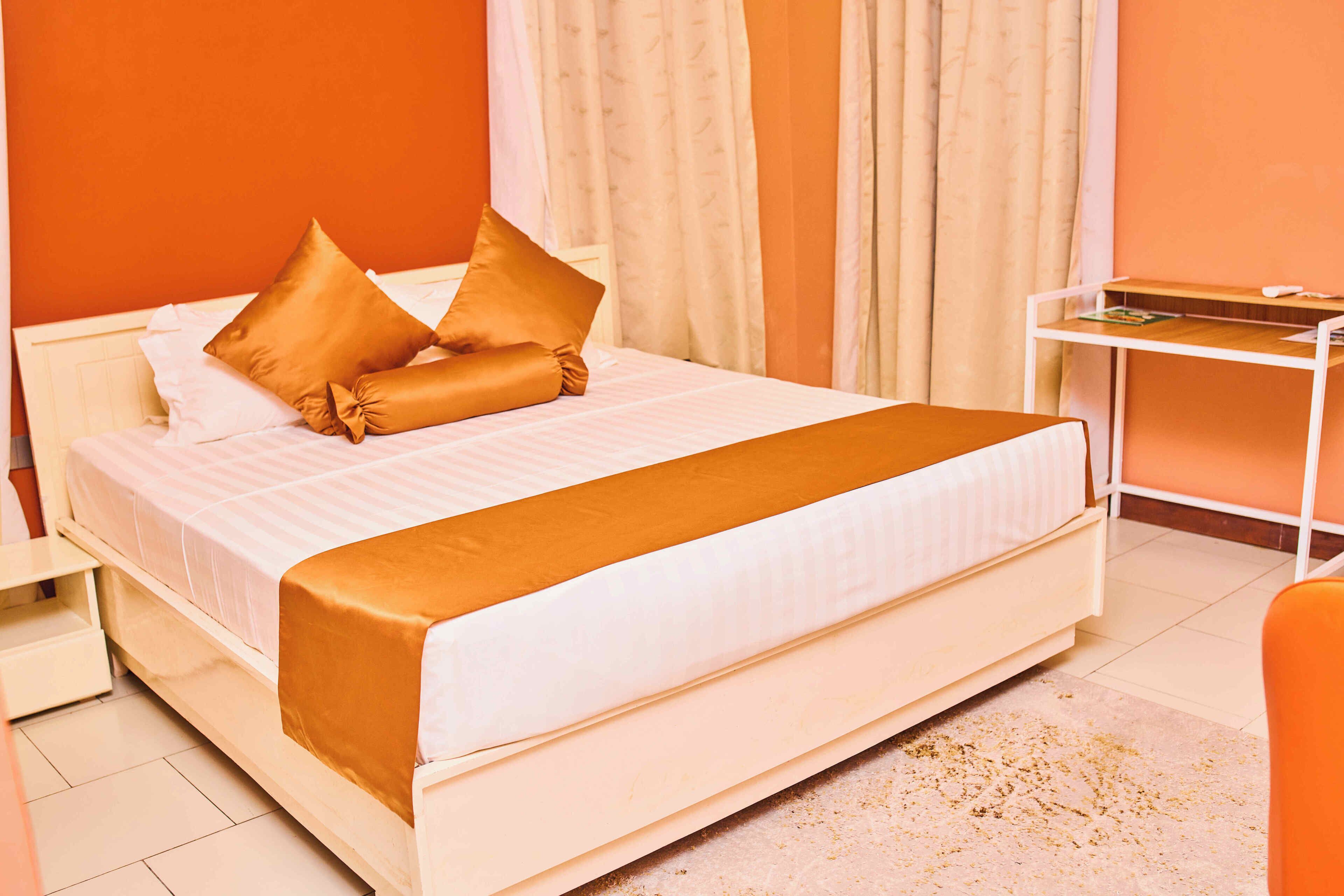 Una cama bien hecha con una colcha blanca y marrón, una mesita de noche blanca y un escritorio pequeño con una silla.