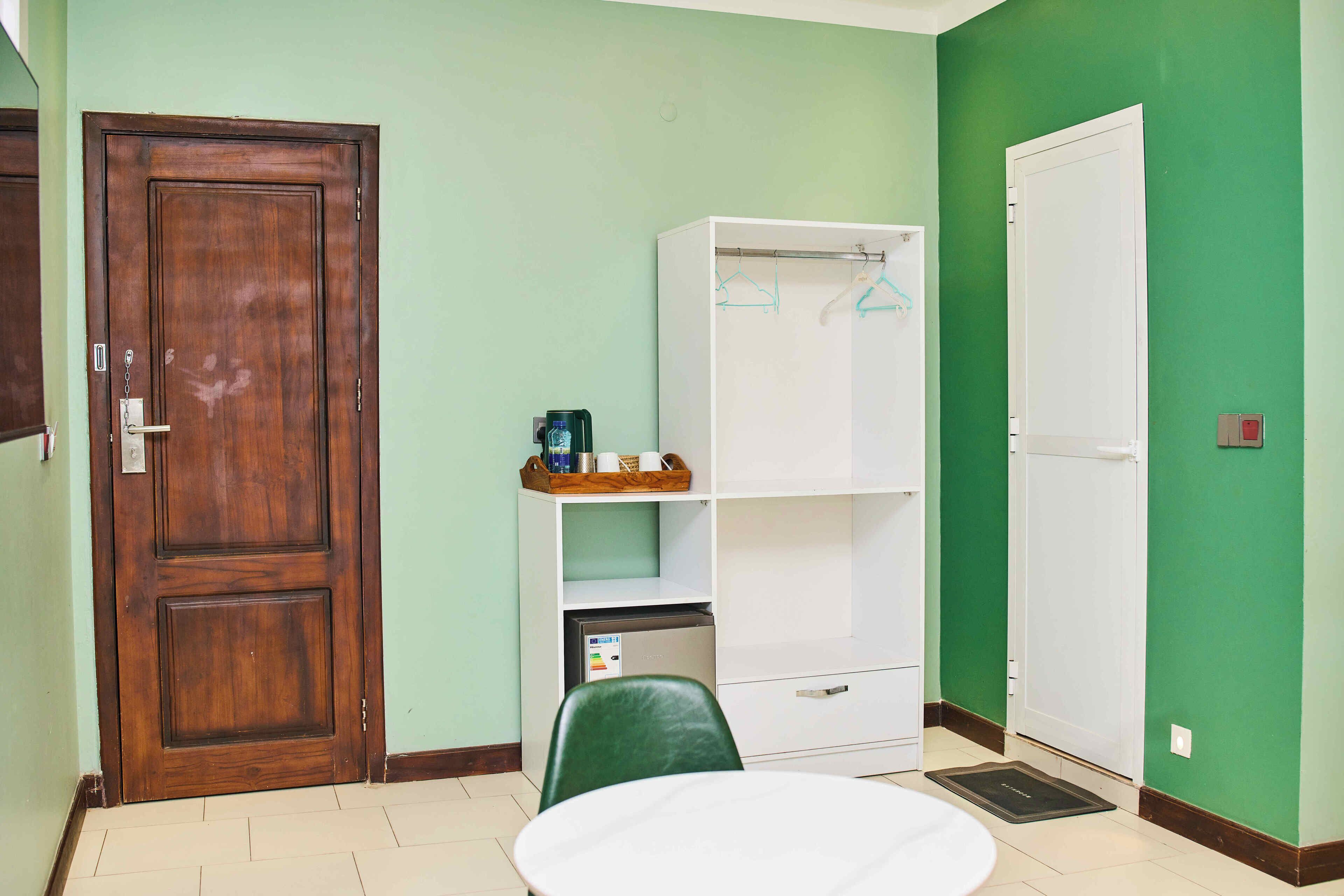 A room with a wooden door, a white wardrobe, a green chair, and a small table.