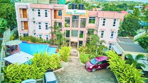 A multi-story hotel with a swimming pool, surrounded by lush greenery and a parked van. - Hotel Amaranth (Dar es Salaam)