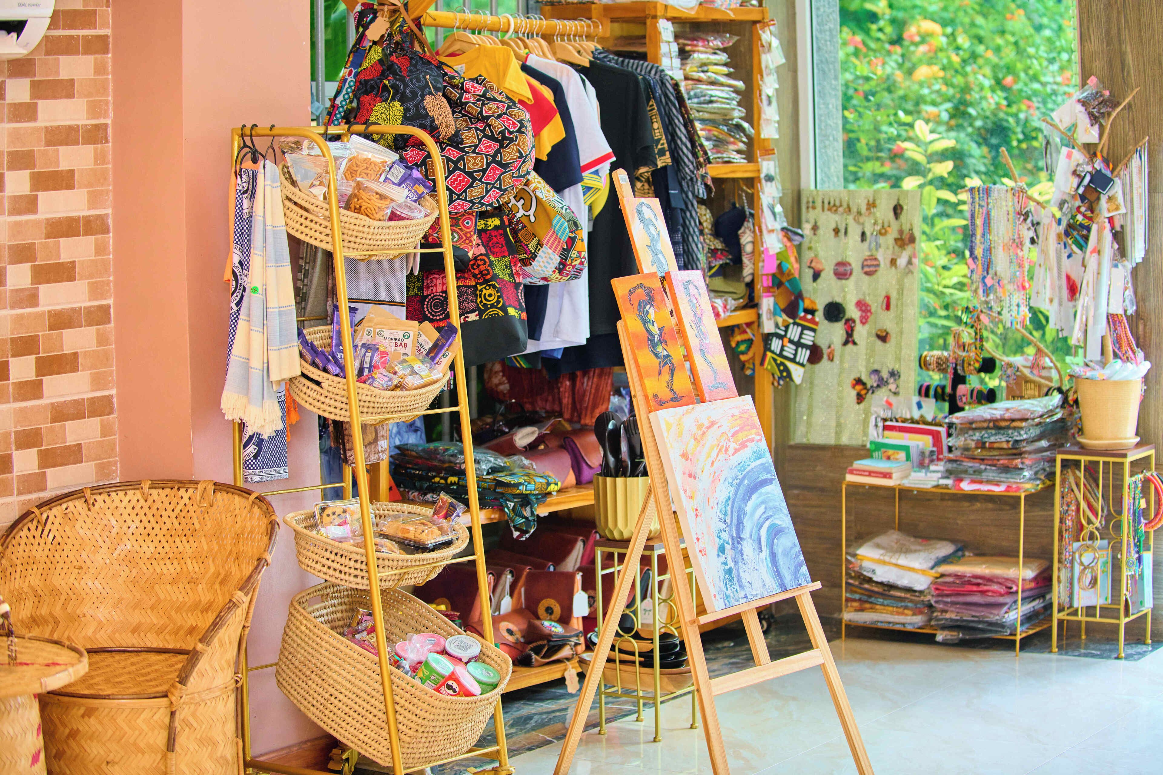 A room with a wicker chair, a wooden shelf with textiles, and a painting on display.