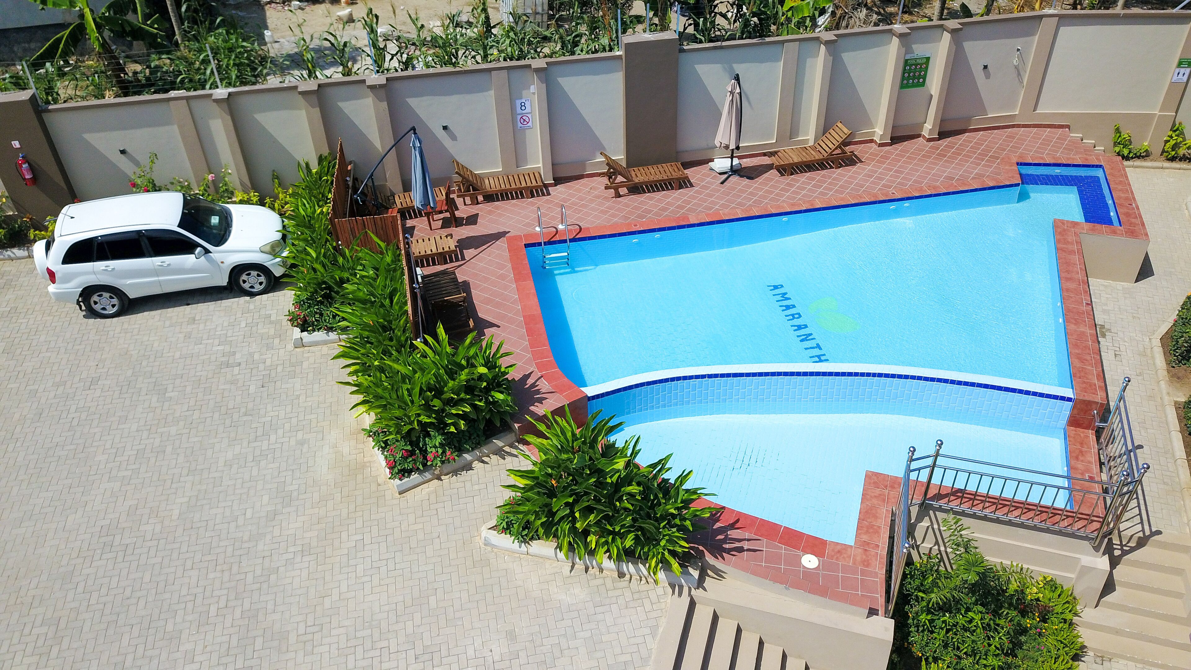 Una piscina con borde de baldosas, rodeada de sillas de descanso y plantas en macetas.