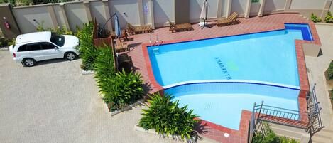 A swimming pool with a tiled deck, surrounded by lounge chairs and potted plants.