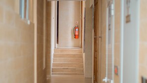 A hallway with wooden flooring, a fire extinguisher mounted on the wall, and a door on the right side. - Hotel Amaranth (Dar es Salaam)