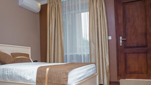 A bedroom with a bed, curtains, a door, and an air conditioning unit. - Hotel Amaranth (Dar es Salaam)