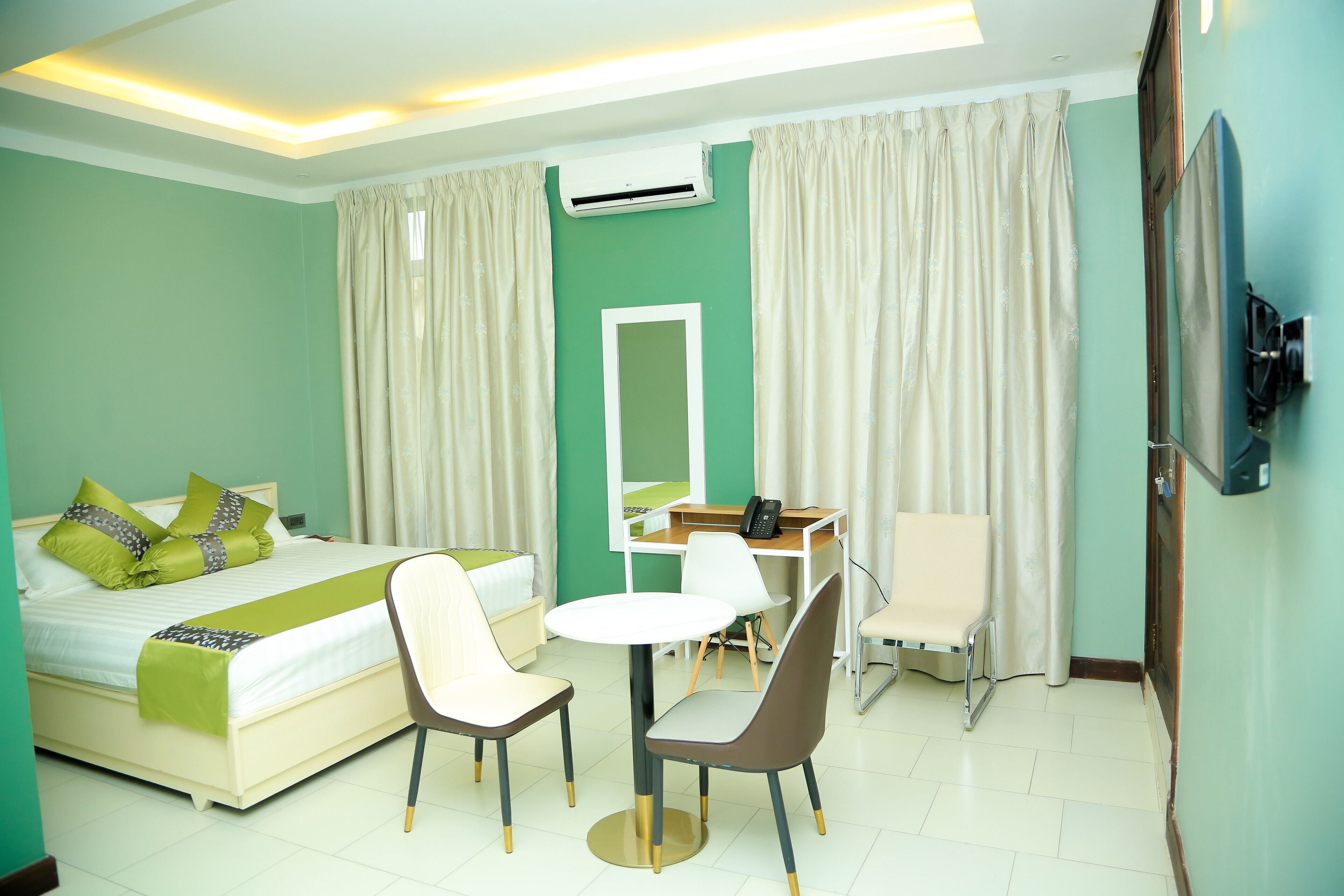 Habitación de hotel con cama, escritorio, silla, televisor y espejo.