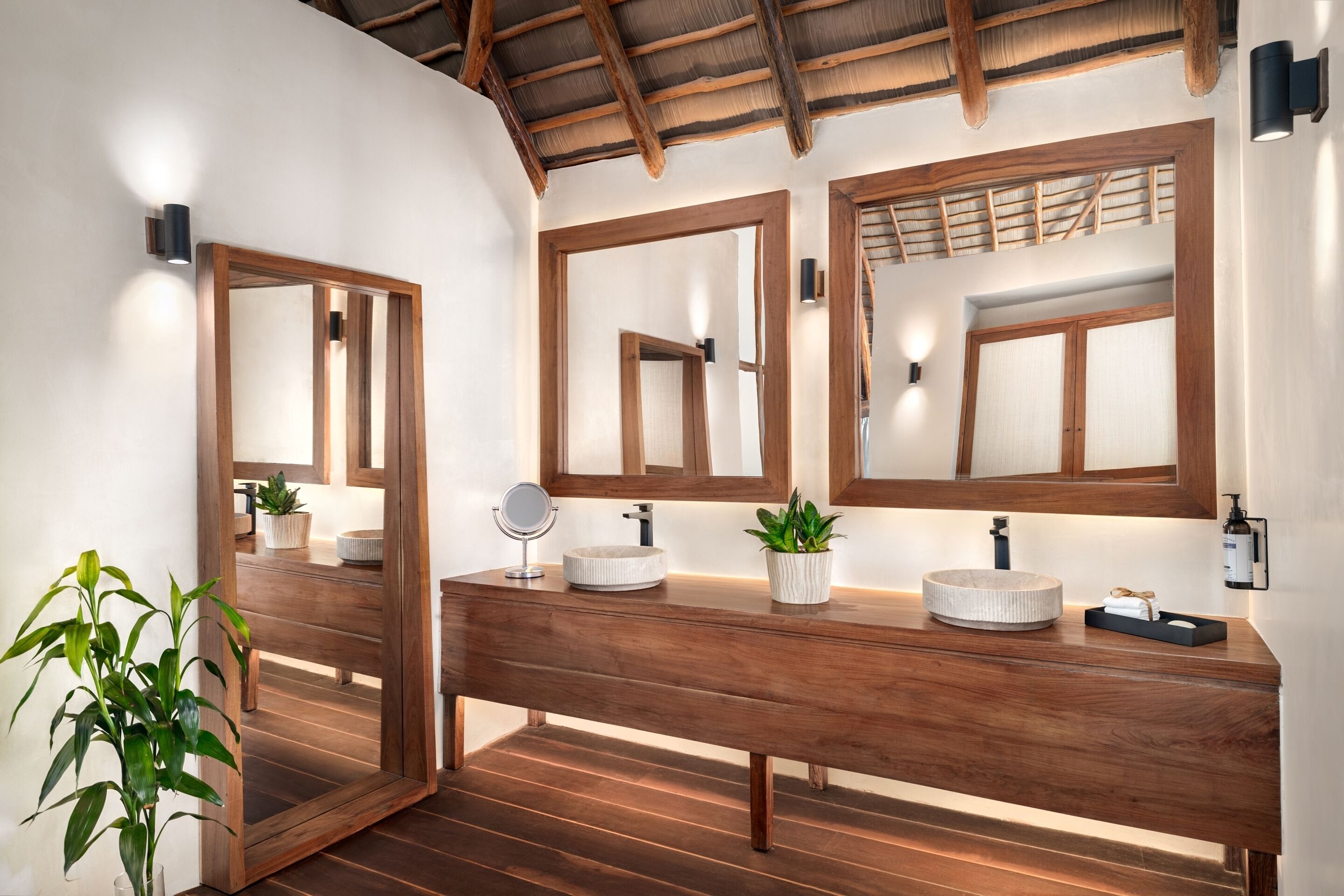 Un tocador de madera con dos espejos, un lavabo redondo y una pequeña planta en maceta.