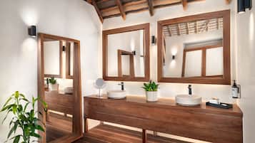 Un tocador de madera con dos espejos, un lavabo redondo y una pequeña planta en maceta.