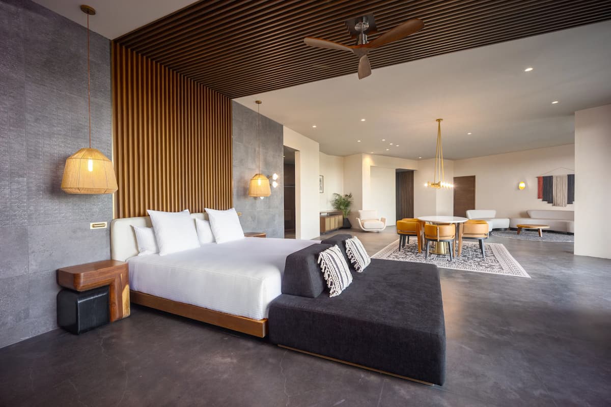Un dormitorio moderno con una cama grande, mesitas de noche, un sofá y una zona de comedor con sillas y una mesa.