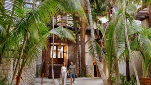 A couple walking on a stone pathway surrounded by palm trees and a stone wall. - Secrets Tulum Resort & Beach Club - Adults Only - All Inclusive (Tulum)