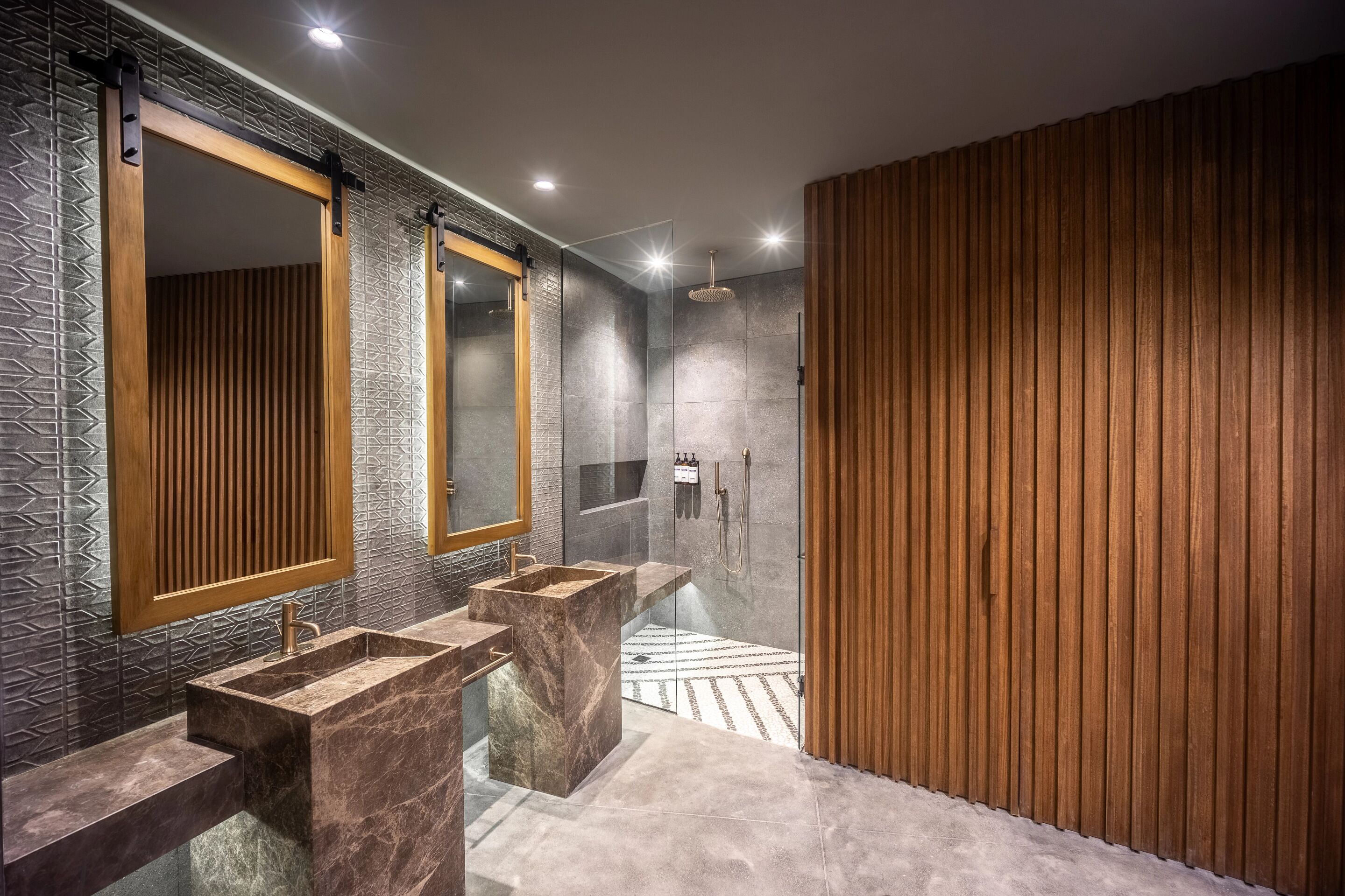 A modern bathroom with a large mirror, two sinks, and a shower area.