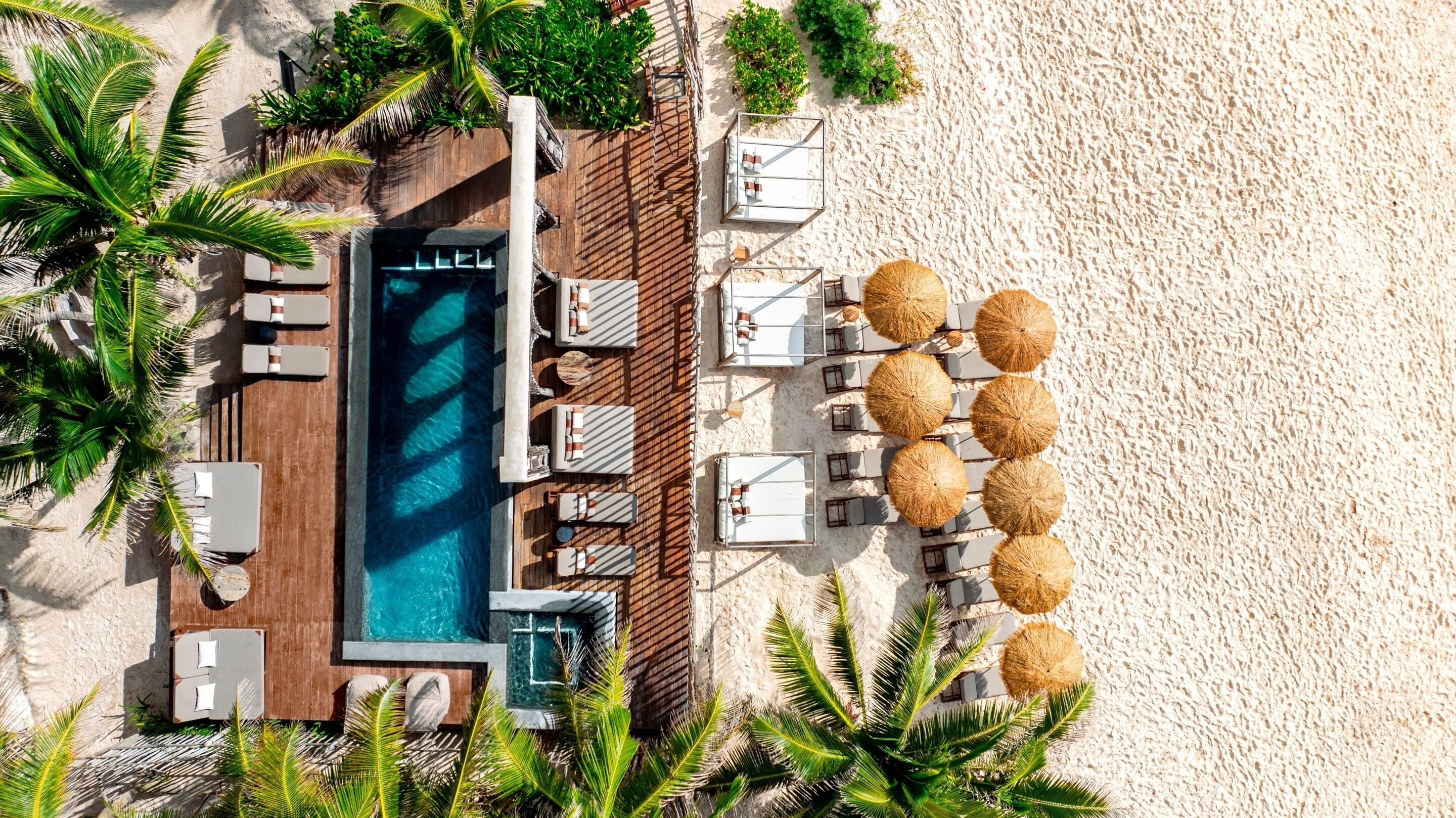 An aerial view of a beachside resort with a swimming pool, sun loungers, and umbrellas.