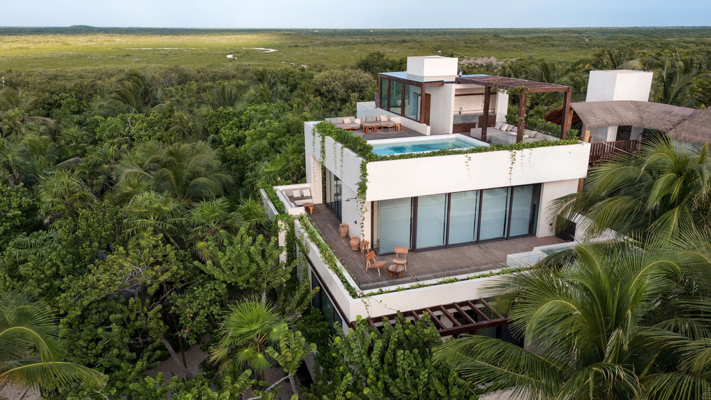 A modern villa with a rooftop pool, surrounded by lush greenery and palm trees.