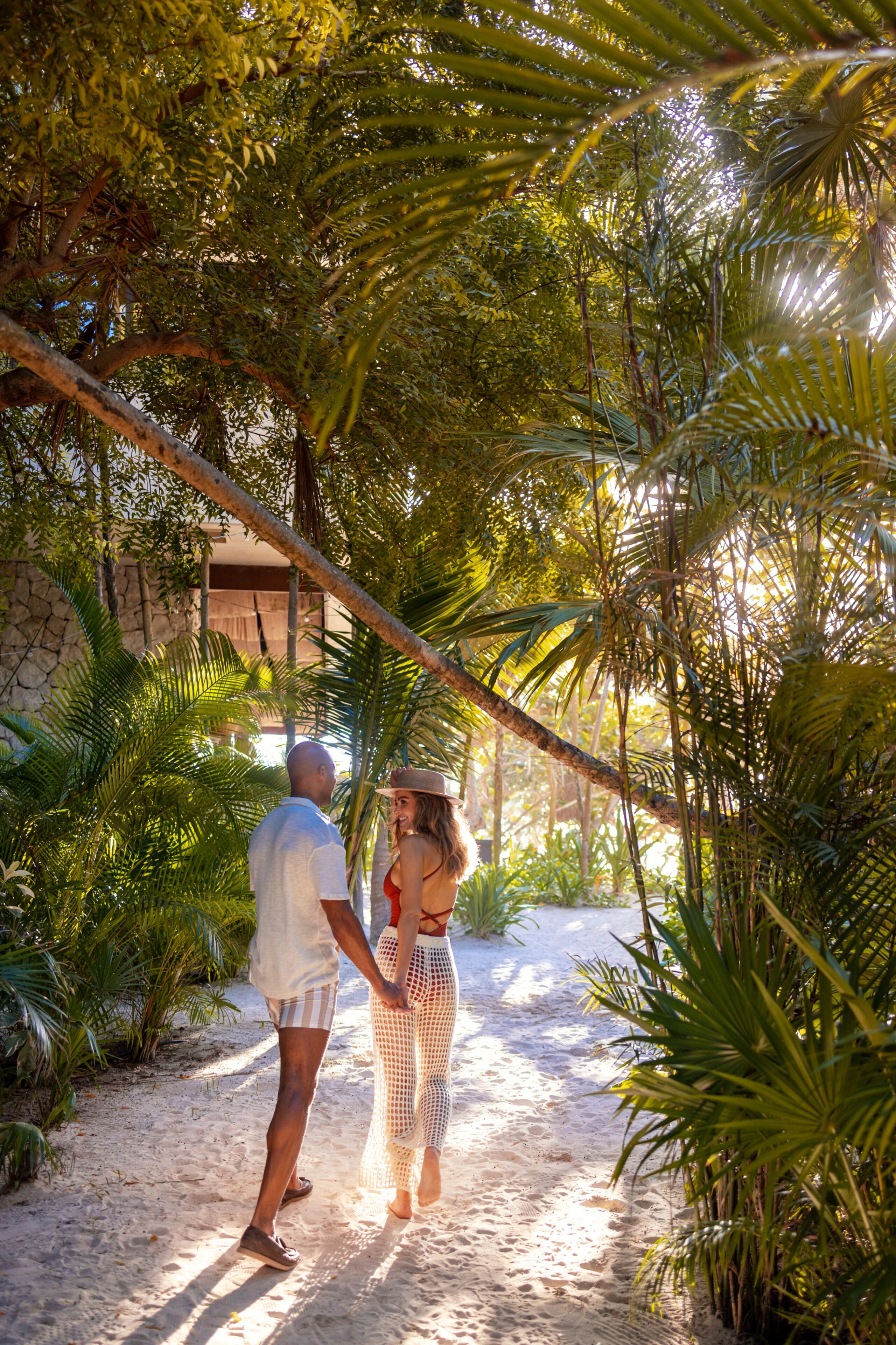 A couple walking on a sandy path surrounded by lush greenery.
