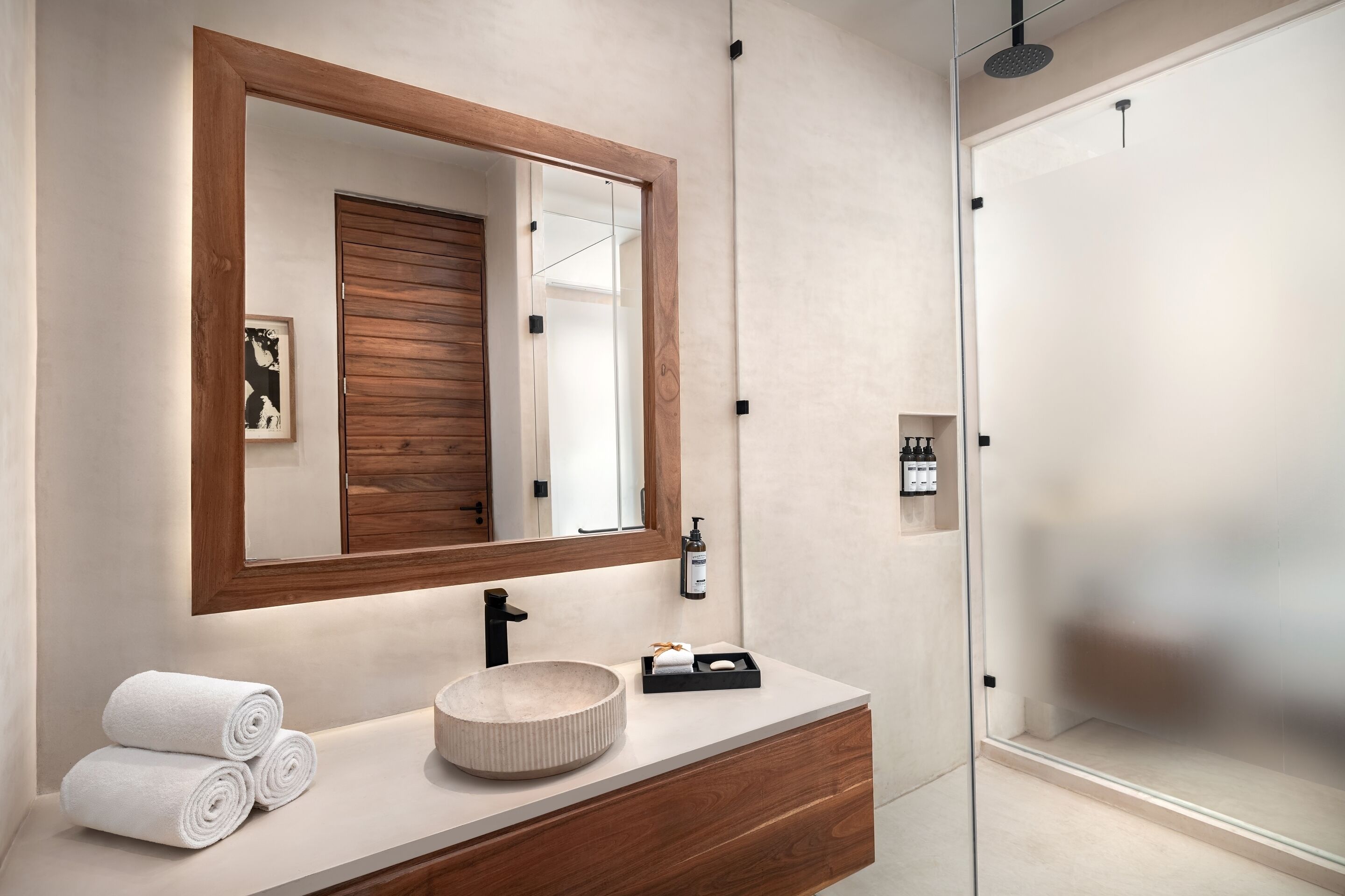 A modern bathroom with a wooden vanity, a large mirror, and a glass shower enclosure.