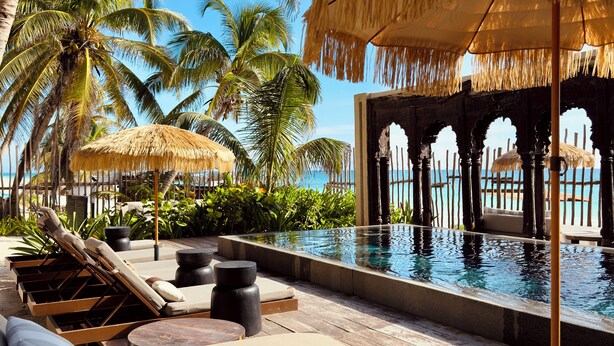 A poolside area with lounge chairs, a thatched umbrella, and a view of the ocean. - Secrets Tulum Resort & Beach Club - Adults Only - All Inclusive (Tulum)