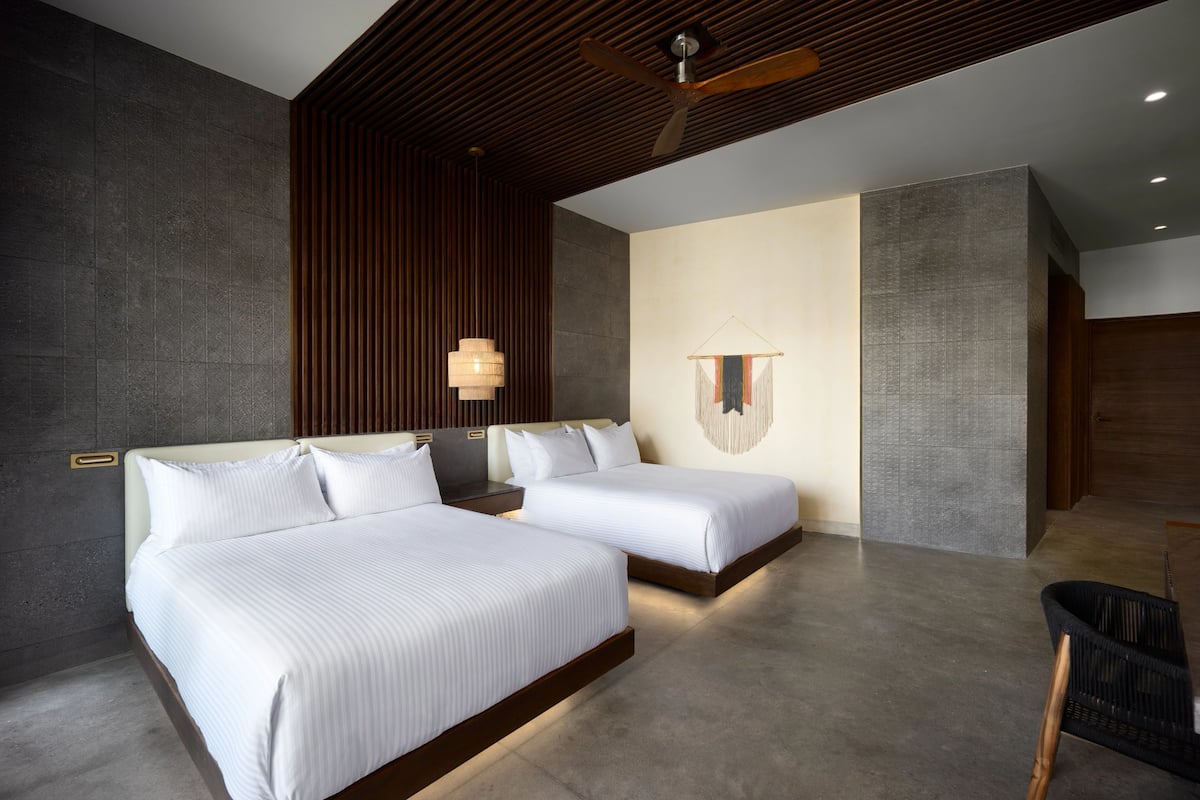Una habitación de hotel moderna con dos camas, techo de madera y pared con textura.