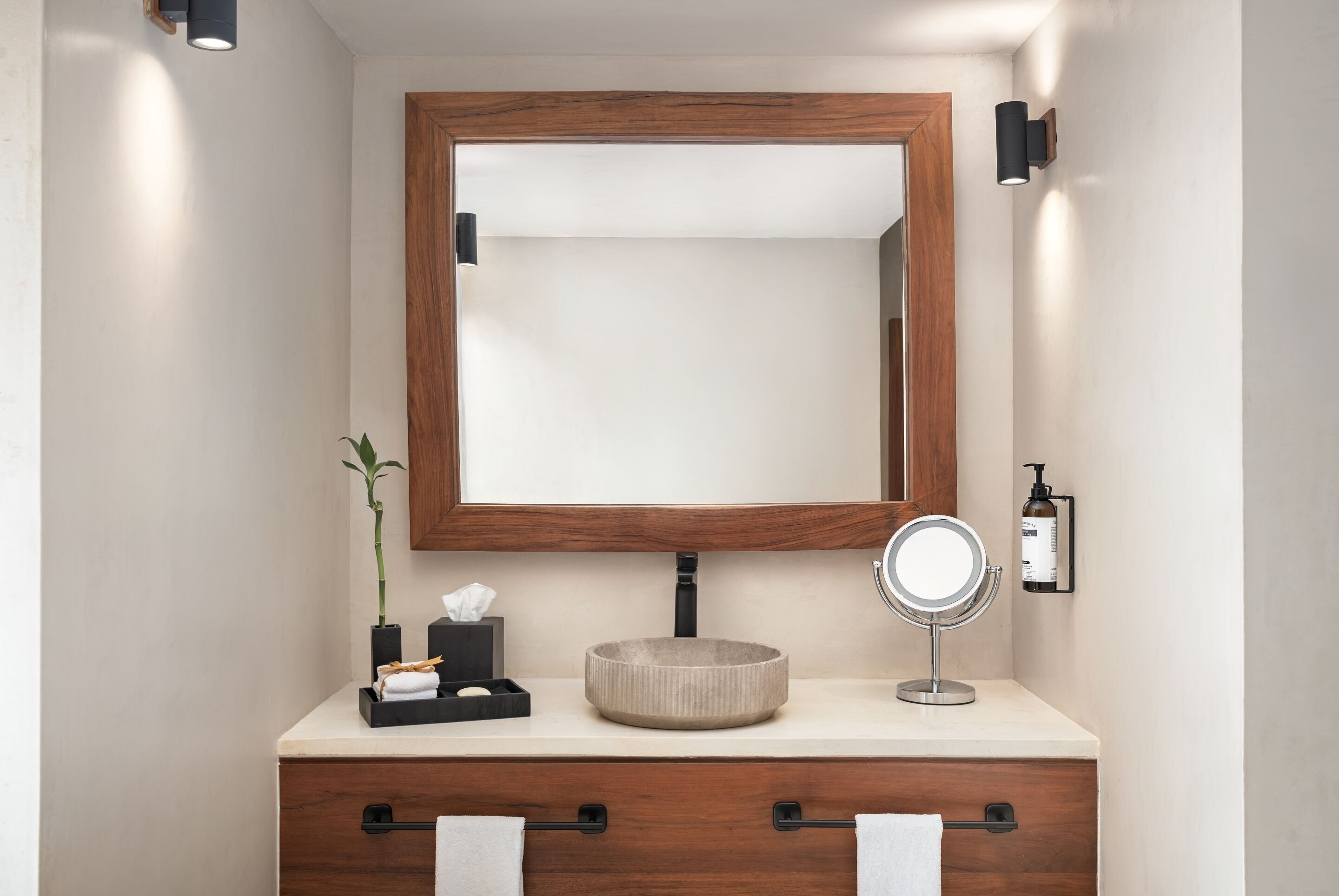 A bathroom with a wooden vanity, a round mirror, and a small potted plant.